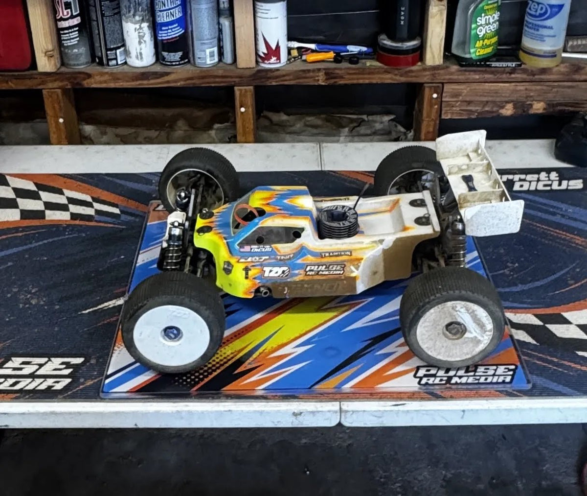 RC buggy displayed on a custom pit board with orange, blue, and white graphics