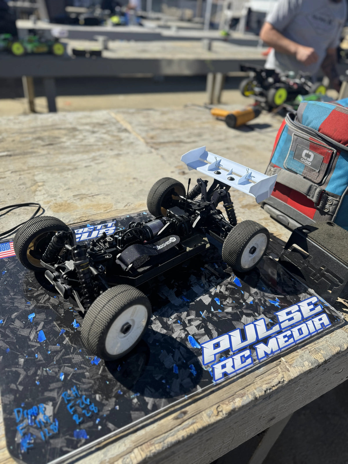 RC buggy chassis on a blue and black custom pit board at the track