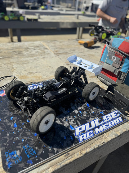 RC buggy chassis on a blue and black custom pit board at the track